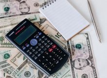 calculator and notepad placed on usa dollars stack