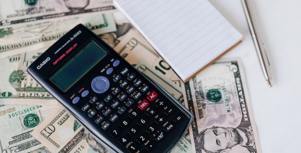 calculator and notepad placed on usa dollars stack